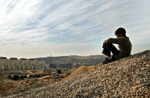 A Palestinian boy from Bilin outside Ramallah sits over an Israeli settlement being constructed next to the village, December 2005. Image courtesy www.electronicintifada.net. Photo credit: Charlotte de Bellabre/MaanImages.